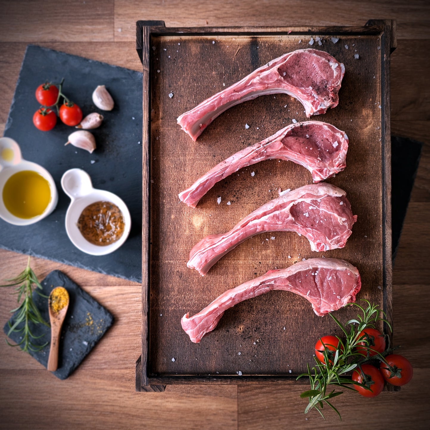 Raw lamb chops on a wooden tray with herbs and spices on a wooden surface