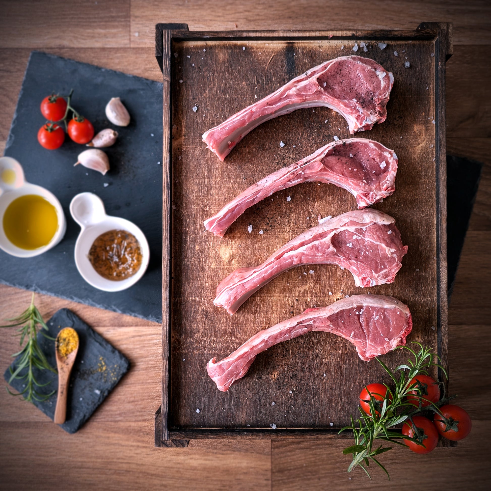 Raw lamb chops on a wooden tray with herbs and spices on a wooden surface