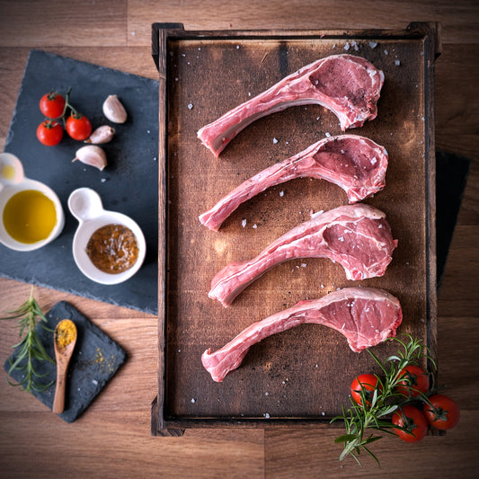 Raw lamb chops on a wooden tray with herbs and spices on a wooden surface